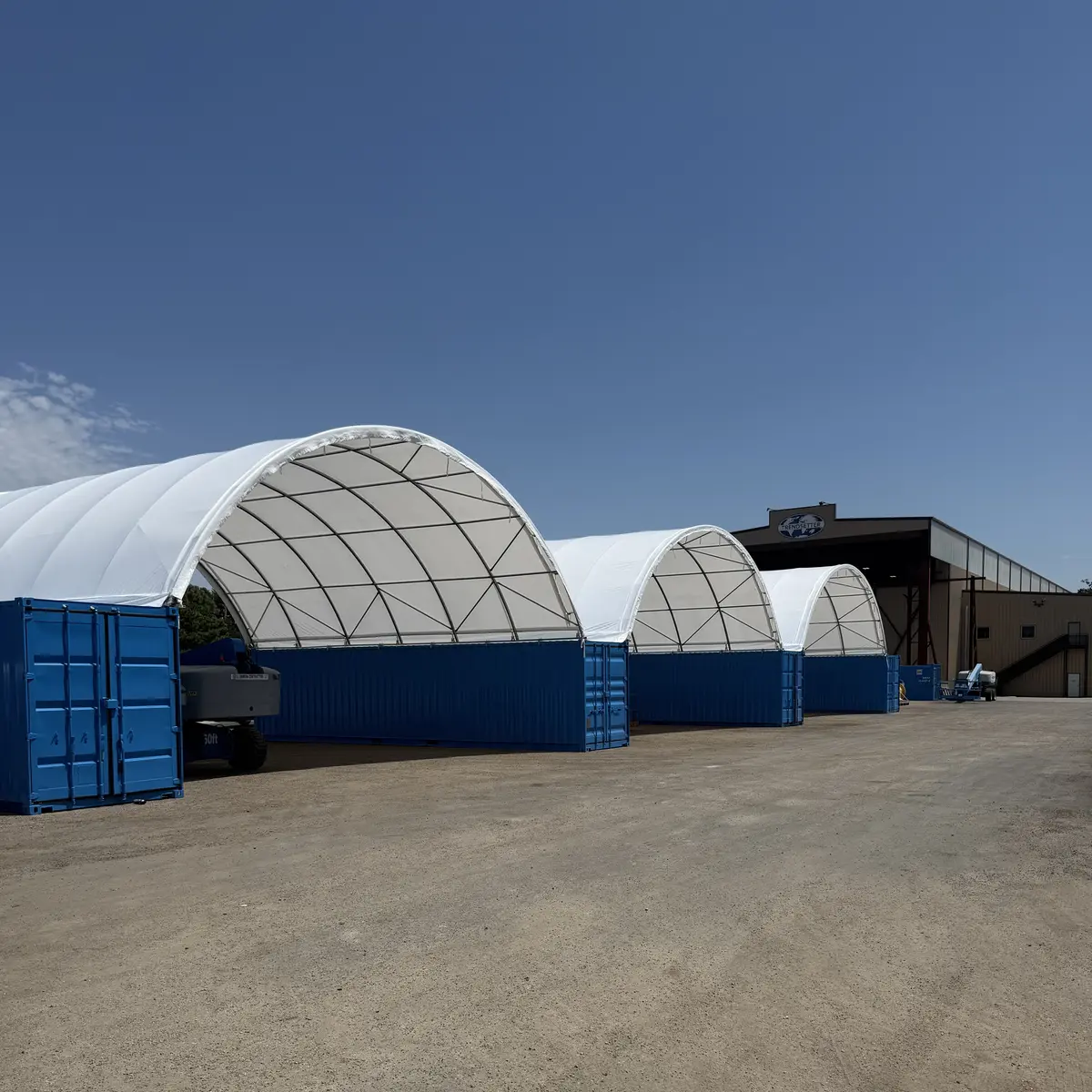 Side view of three white fabric shipping container canopy shelters mounted on blue containers